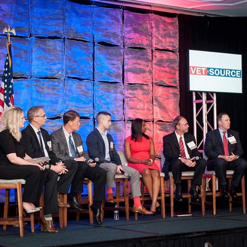 Panel of seven people sitting on a stage in chairs